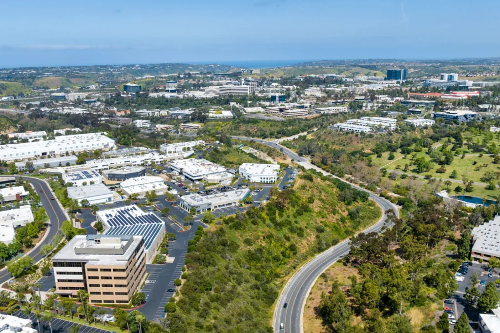 An aerial view of commercial buildings and green hills near luxury hotels in La Jolla reaching toward the ocean.