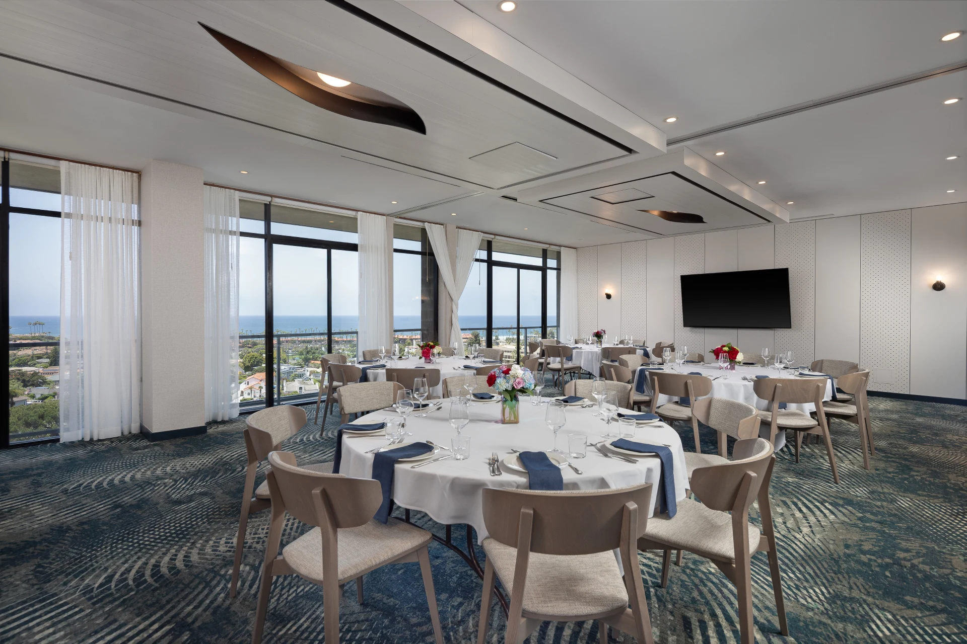 This La Jolla event venues space features round tables set for a banquet with floor-to-ceiling ocean views.