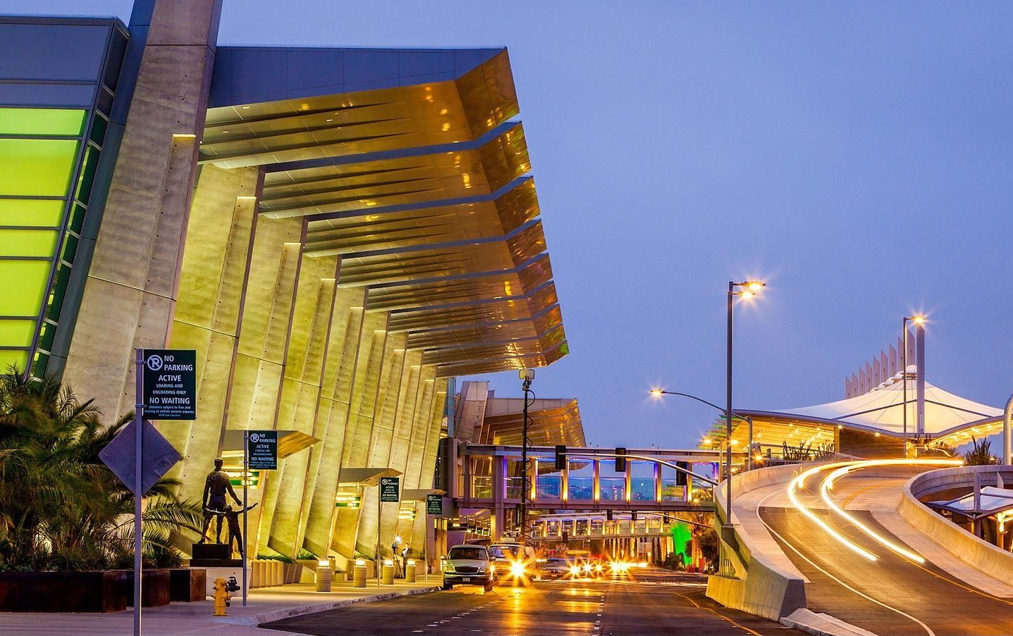 Illuminated modern airport architecture with motion blur from cars driving on an elevated ramp at night.