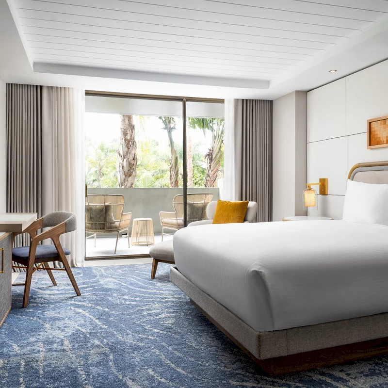 This boutique hotel room features a plush bed and a private balcony overlooking palm trees.