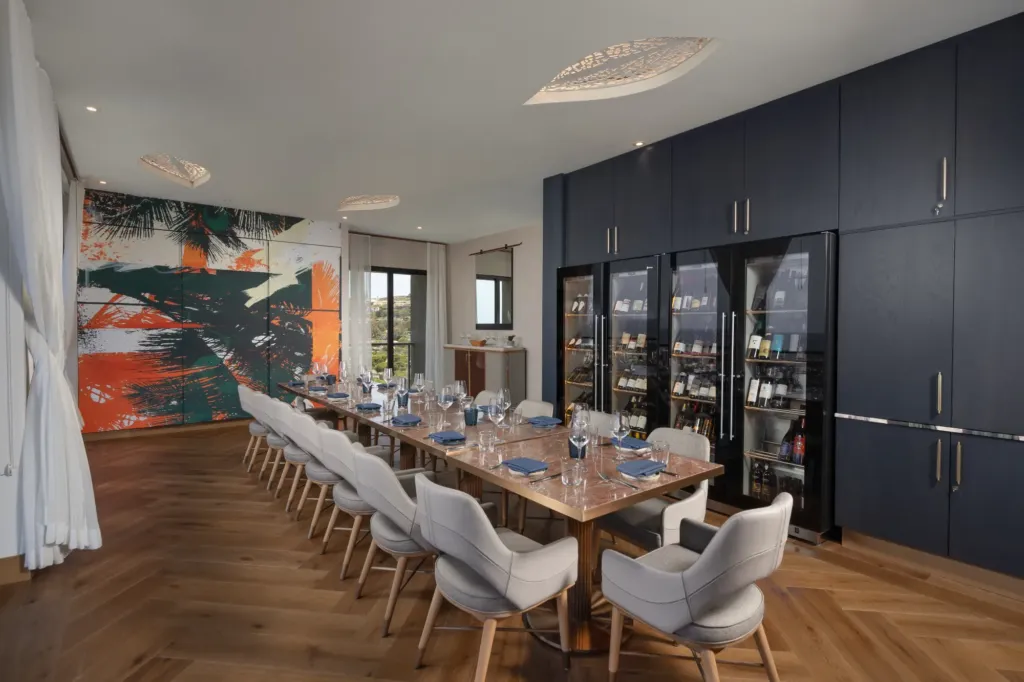 A modern private dining room with a long table set for a group, a full wall of built-in wine refrigerators, and large abstract art